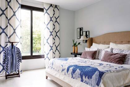 Cama con cabecera capitoné tapizada en lino. Cubrecama blanco con almohadones de diferentes tamaños (todo de Didot). Acompañando la mesa de luz negra, díptico de Agustina Núñez (Diderot Art).