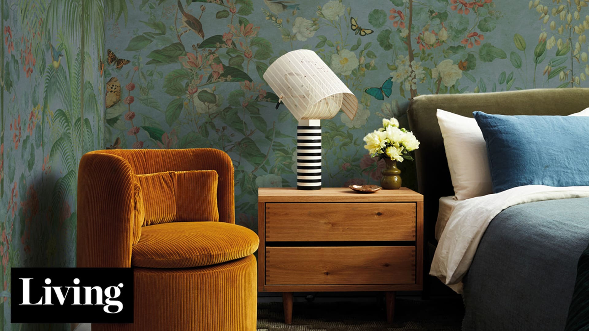Foto de un dormitorio con empapelado, sillón amarillo y cubrecama azul.