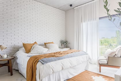 Mesas de luz y sillón (Eugenio Aguirre). Alfombra (Seara). Ropa de cama (Mercer). Pared pintada de blanco ‘Meditación’ (Alba). Velador (Talleres Sustentables). Vela y jarra de noche (Me Copa). Cortinas (Estudio LODD).