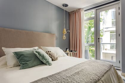 Respaldo de lino contra la pared pintada en ‘Morning Fog’. Mesa (Landmark). Almohadones y acolchado (Belgika). Cortinas dobles de gasa y pana.