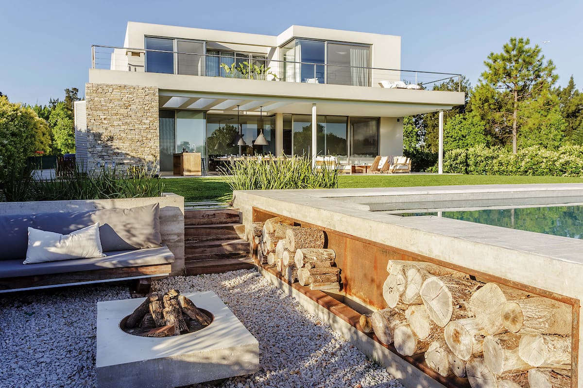 Foto de un jardín con con leñero a mano con fondo de chapa óxido sobre el lateral de la pileta.