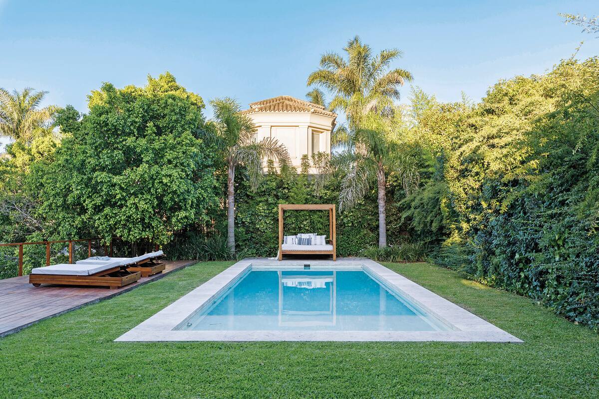 Foto de un jardín con pileta, sillón y reposeras.
