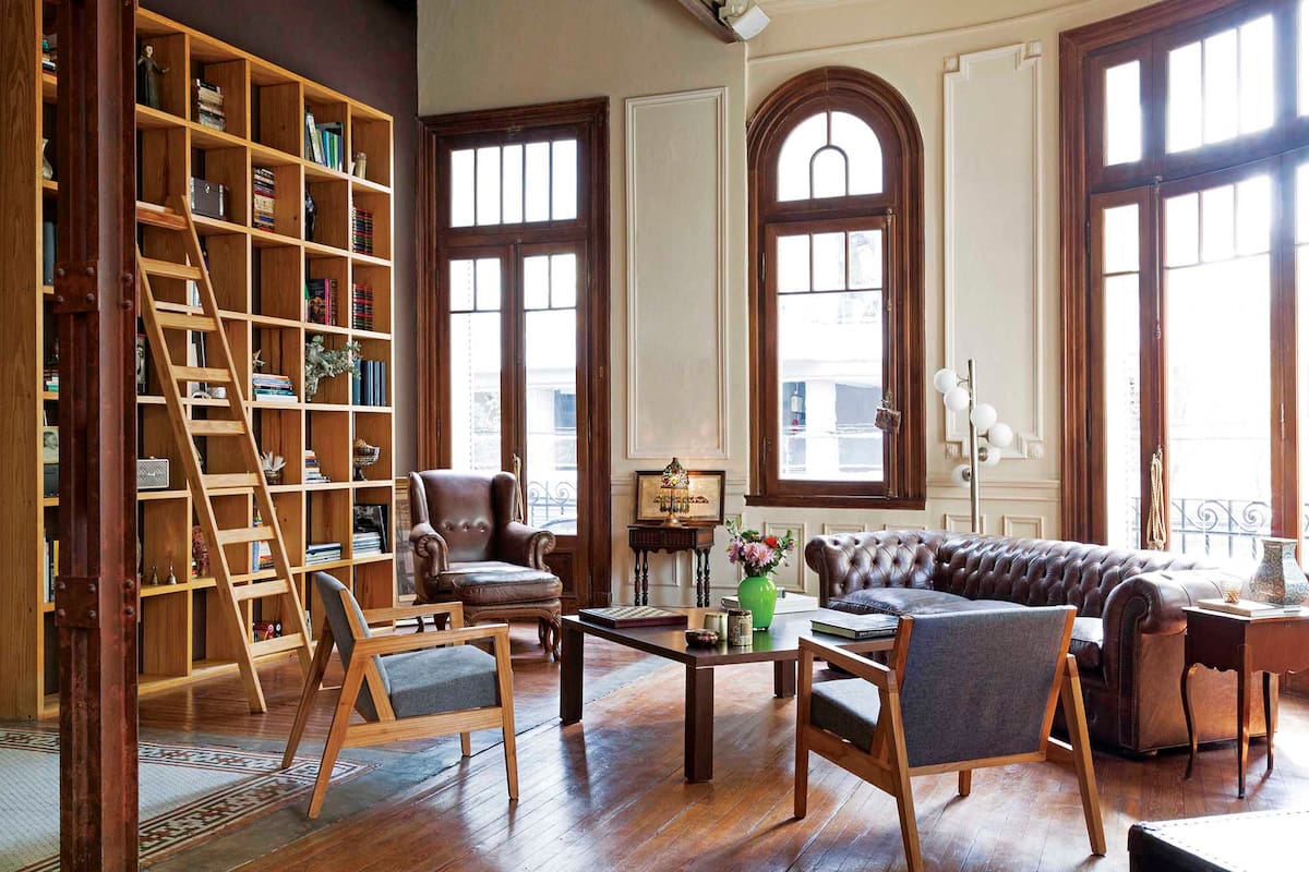 Foto de un living con sillón chester, biblioteca de piso a techo y piso de pino tea.