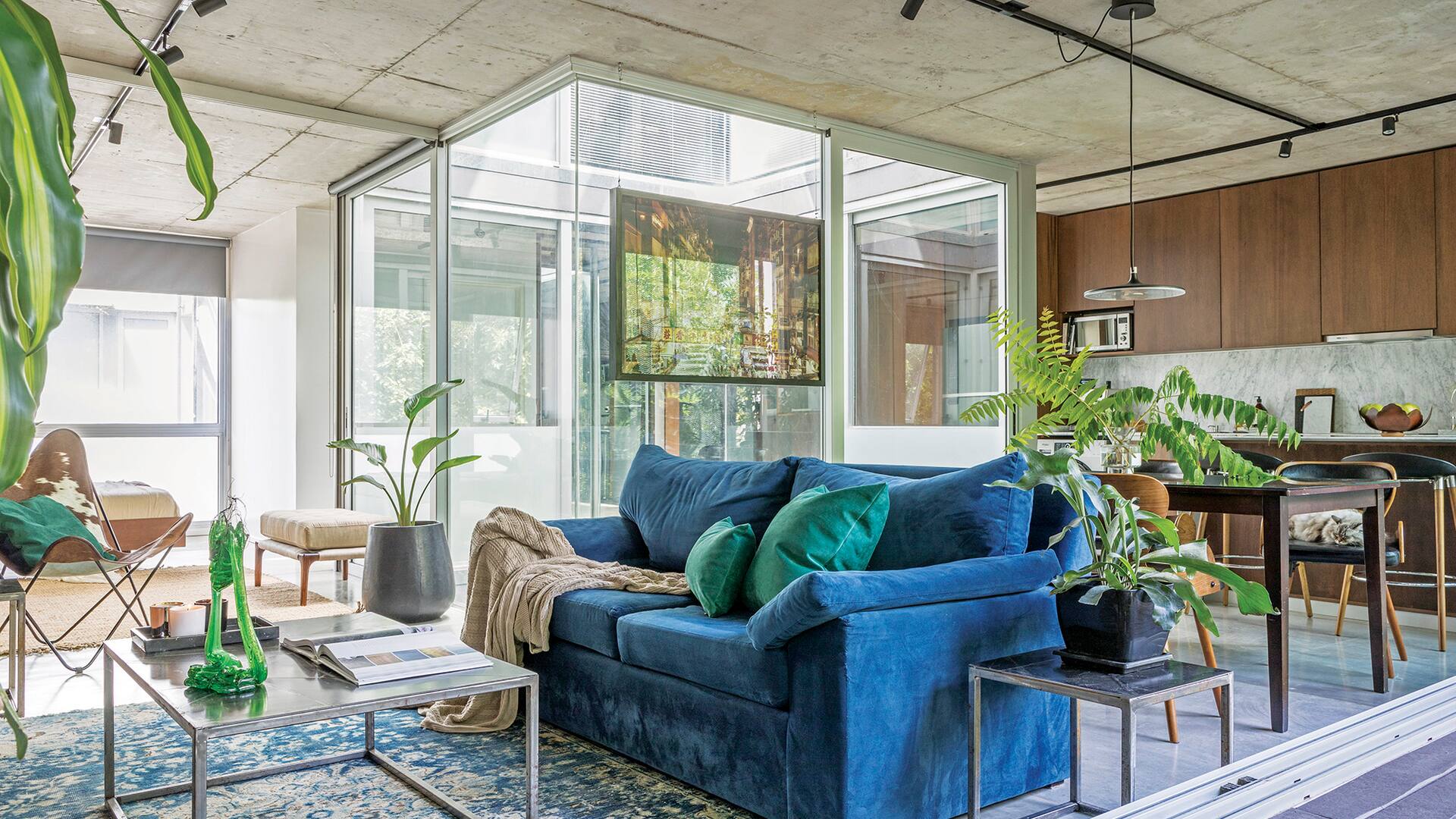 Foto de un living con sillón de pana azul, almohadones de pana verde y manta. Alfombra y mesas de apoyo y de centro.