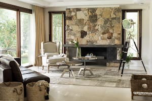 Foto de un living con sillón ‘Marseilles’ de roble platinado y lino, sofá ‘Lincoln’ de cuero, mesas ratonas de altura regulable con patas cromadas y tapa de roble, y lámpara trípode sobre alfombra patchwork.