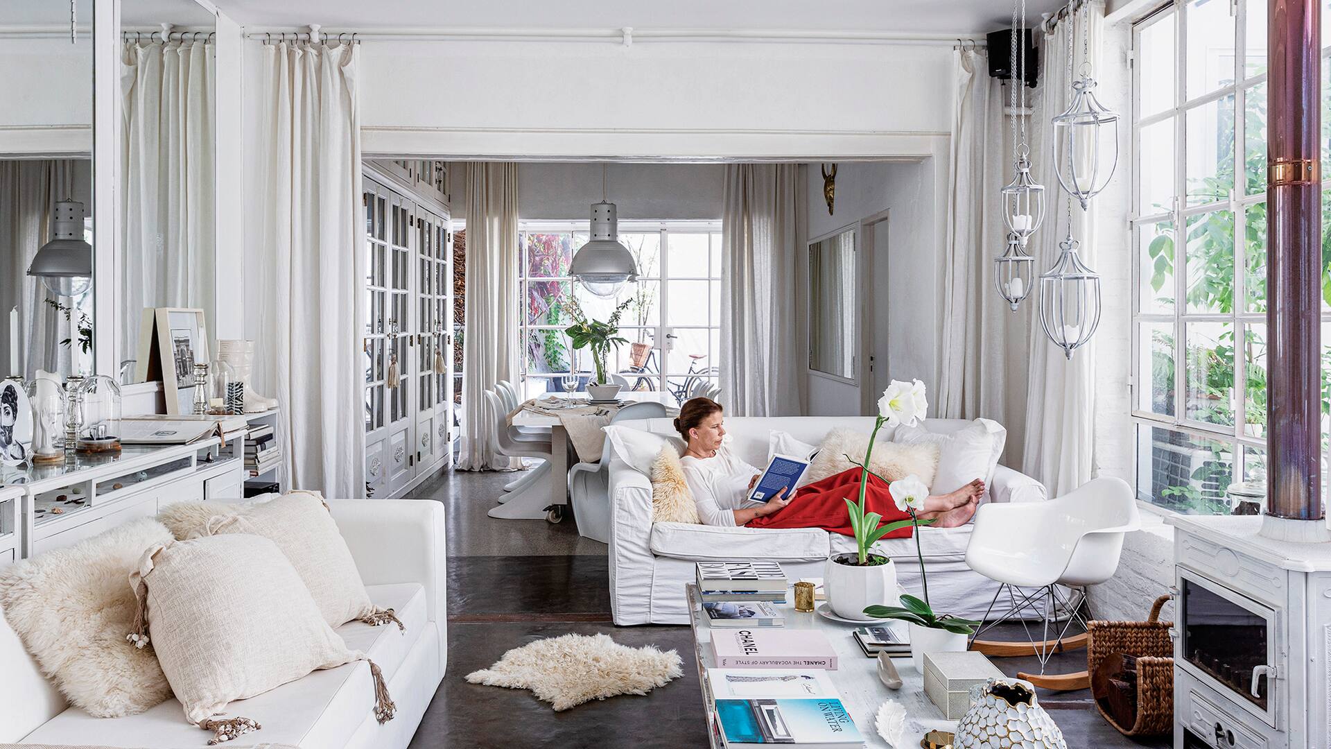 Foto de un living con sillones blancos y salamandra, que se conecta a un comedor con lámparas galponeras.