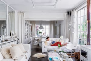 Foto de un living con sillones blancos y salamandra, que se conecta a un comedor con lámparas galponeras.