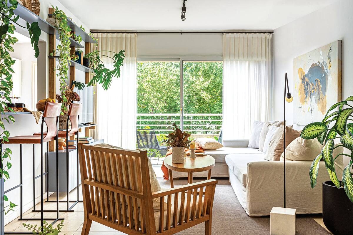 Foto de un living con sofá en L, sillón individual en madera y cortinas de gasa pañalera con barral y argollas negras.