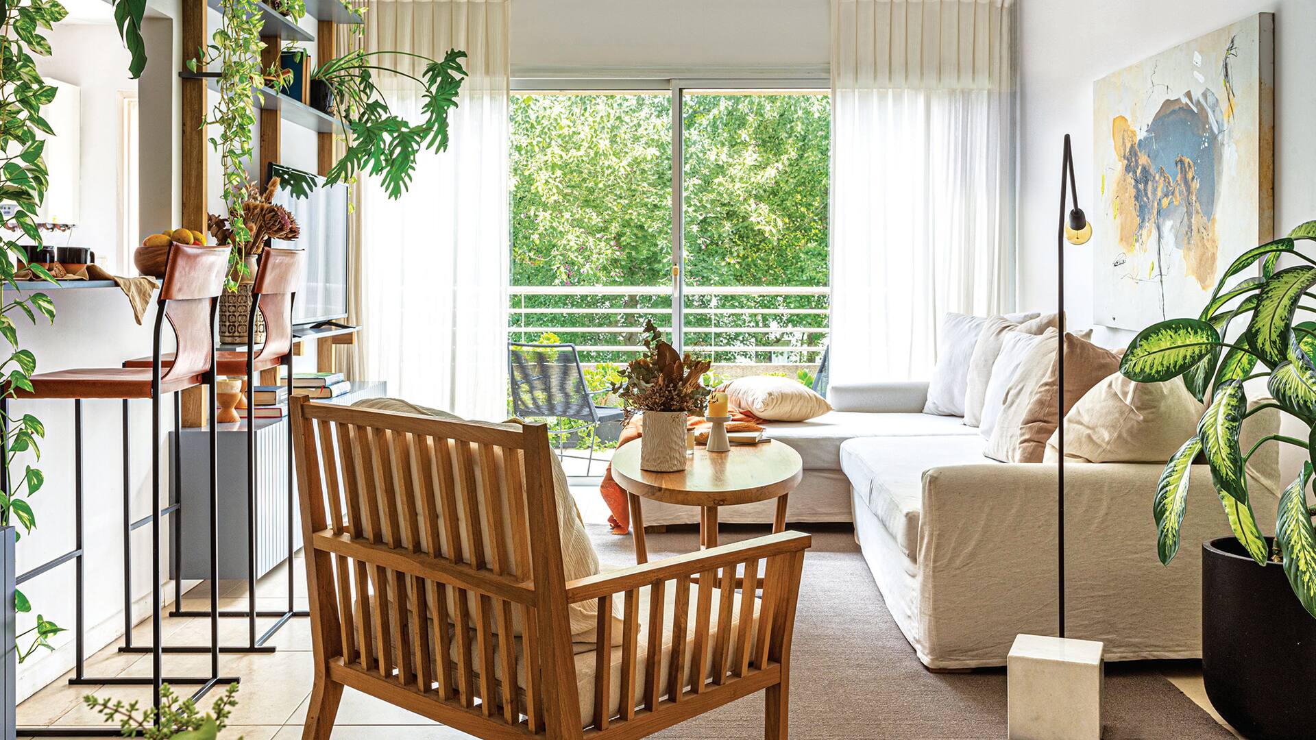 Foto de un living con sofá en L, sillón individual en madera y cortinas de gasa pañalera con barral y argollas negras.