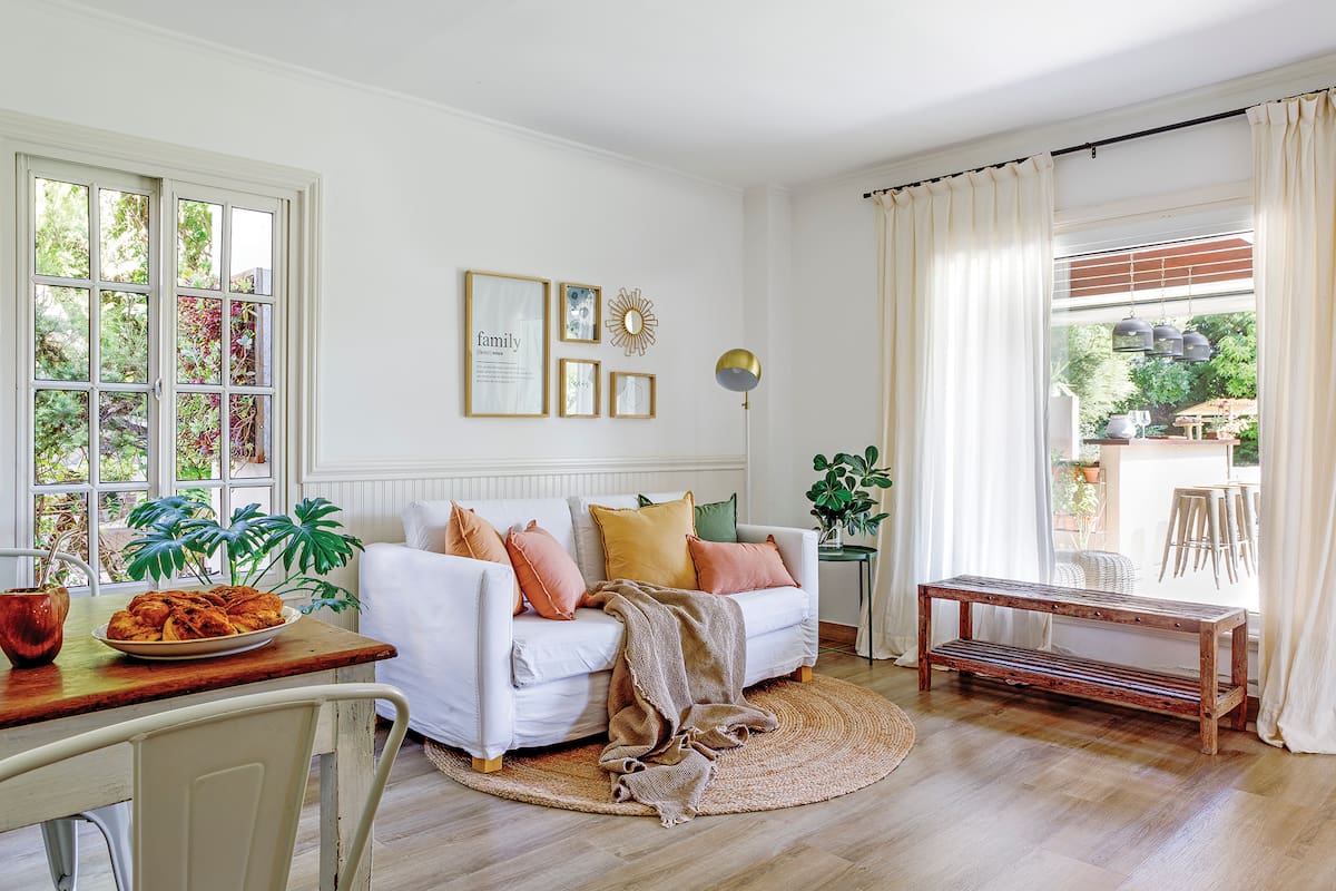 Foto de un living conectado con un comedor diario con sillón, almohadones y manta, alfombra circular de yute, cortinas con barrales y mesa de apoyo.