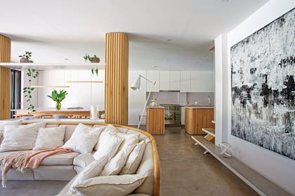 Las columnas revestidas en madera de kiri con estantes, laqueados dividen living de comedor. Lámpara de pie (Manfroni). El cuadro, obra del arquitecto Federico Grizzo, también autor del boceto que abre esta nota.