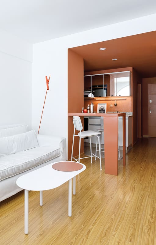 Foto de un living con mesa ratona en balnco, lámpara de pie roja y funda de sillón balnca.