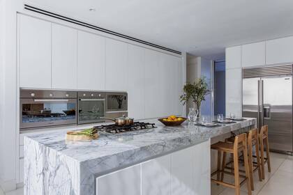 Para completar la pureza de las líneas, se empotraron el anafe, horno eléctrico y a gas y el microondas (todo de Ariston). Banquetas ‘Iguazú’ en petiribí. Los laterales son de laca brillante blanca, como todos los muebles del ambiente.
