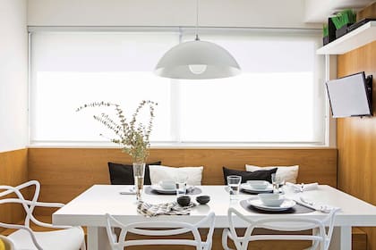 En la cocina, asiento de madera (Estudio Filcman Gurfinkiel), sillas ‘Masters’ (Deco Design) y lámpara colgante (Ikon Iluminación). Sobre la mesa laqueada semimate, individuales de cuero, servilletas de algodón y repasador estampado (todo de Claudia Adorno).