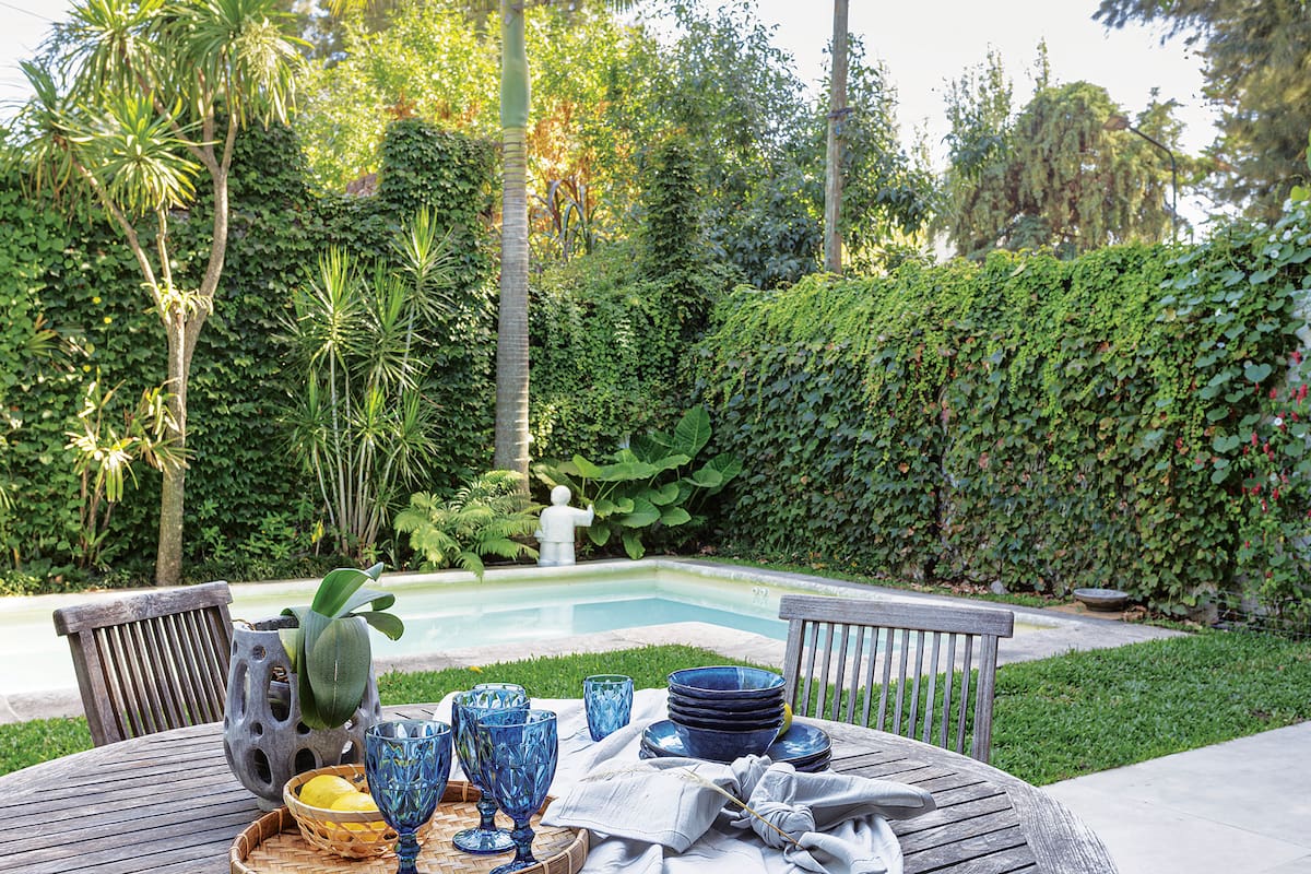 Foto de una mesa de teca. Detrás, una pileta pintada de aguamarina.