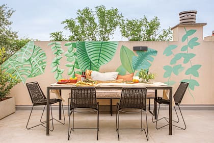 Foto de una terraza con mural, mesa de hierro y banco y sillas tejidas en soga negra.