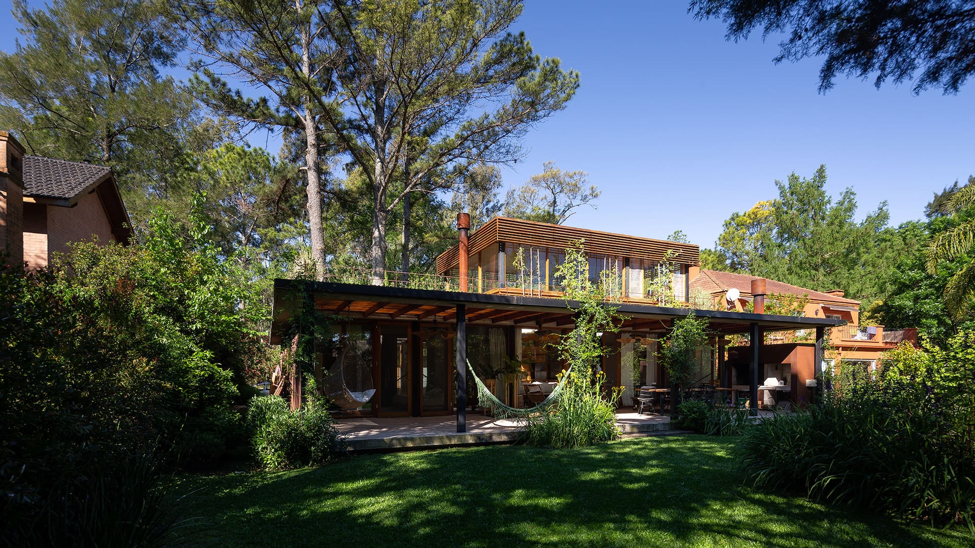 Foto del jardín de una casa con sector parrilla y hamacas.