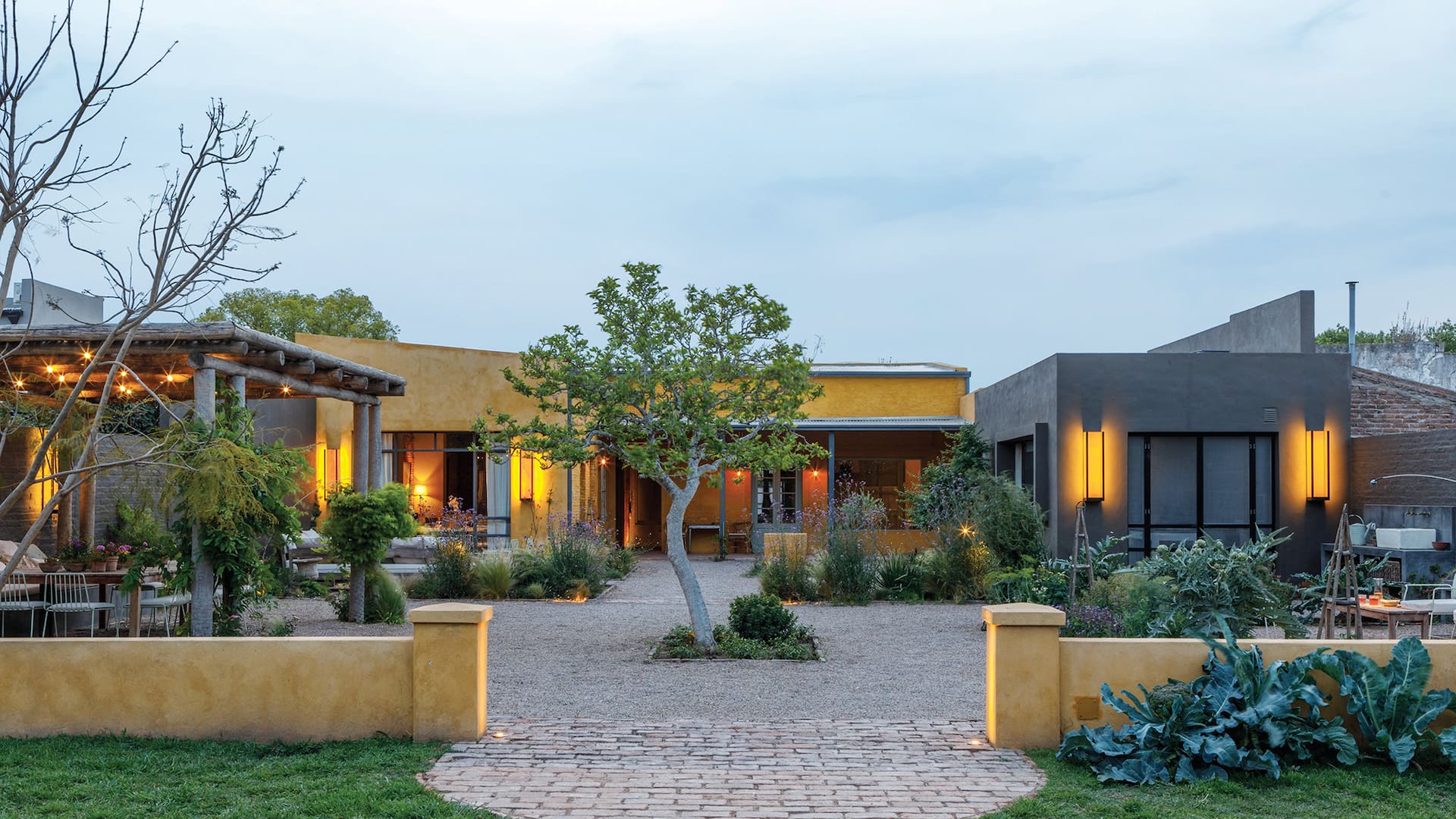 Foto del jardín y la fachada de un restaurante con luces puntuales cálidas y paredes pintadas de amarillo.