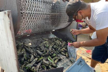 Fotografía del 12 de julio de 2021 de Israel García embolsando chiles verdes asados en un puesto a orillas de la calle en Hatch, Nuevo México. (AP Foto/Susan Montoya Bryan, Archivo)