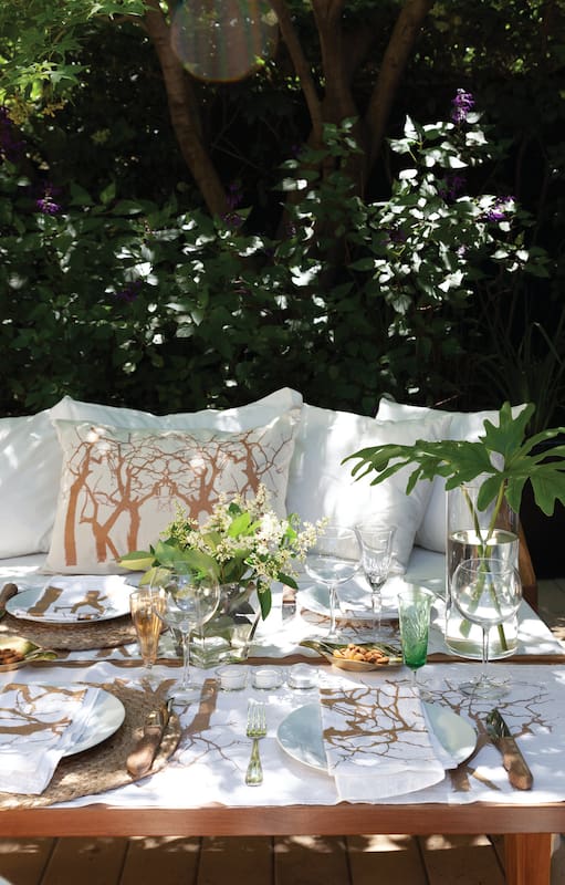Foto de una mesa baja de madera con camino y servilletas en blanco y dorado, velas y bowl dorado.