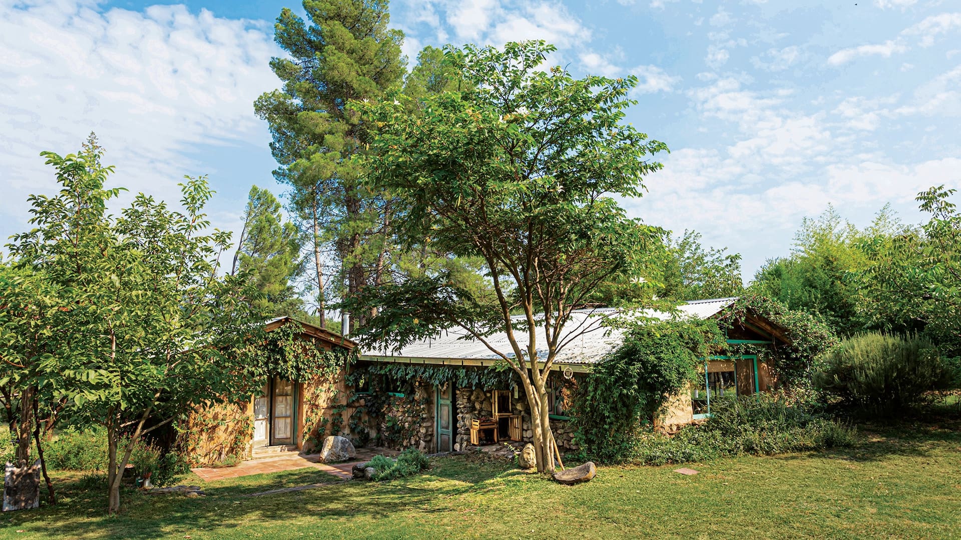 Fresca en verano y cálida en invierno, la casa de adobe y piedra se encuentra parcialmente enterrada (de ahí su mínima transferencia térmica) en el corazón de un inmenso jardín con frutales, aromáticas, huerta y una pileta natural para bañarse entre nenúfares.