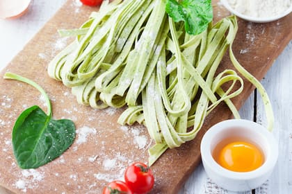 Fresh pasta tagliatelle with spinach leaves, vegetables and eggs on white wooden background, selective focus