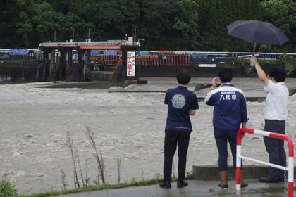 Funcionarios municipales, a orillas del río Kuma, con más caudal del habitual debido a las intensas lluvias, en Yatsushiro, en el sur de Japón, el 30 de agosto de 2024, luego del paso de una tormenta. (Hidetaka Komukai/Kyodo News via AP)