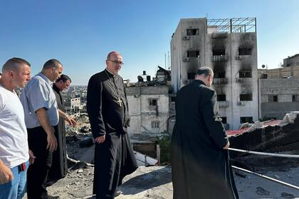 Gabriel Romanelli, párroco de Gaza, de espalda, junto al patriarca Pizzaballa; de fondo, la destrucción de Gaza