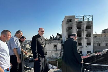 Gabriel Romanelli, párroco de Gaza, de espalda, junto al patriarca Pizzaballa; de fondo, la destrucción de Gaza