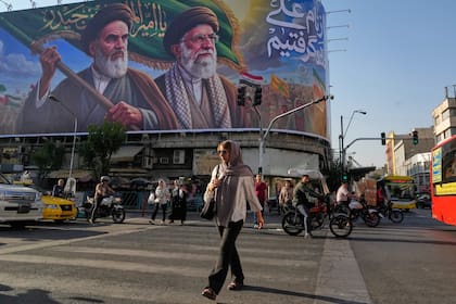 Gente camina bajo una pancarta con retratos del fallecido fundador de la Revolución Islámica, el ayatolá Khomeini, y el fallecido líder supremo Alí Khamene