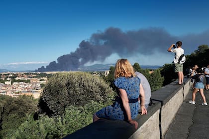 Gente en la Piazza Garibaldi, en la colina de Gianicolo, mira el humo que se eleva después de que estalló un incendio cerca del parque arqueológico del distrito de Centocelle, en el este de Roma