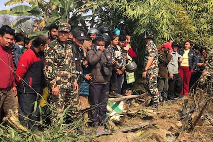 Gente mirando los restos de un avión de pasajeros accidentado en Pokhara, Nepal, el domingo 15 de enero de 2023. Un avión de pasajeros con 72 personas a bordo se estrelló cerca del Aeropuerto Internacional de Pokhara, en Nepal, según el diario Kathmandu Post. (AP Foto/Ashish Puri)