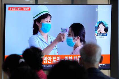 Gente mirando una pantalla de televisión que muestra un reporte noticioso sobre el brote de COVID-19 en Corea del Norte, en una estación de tren de Seúl, Corea del Sur, el sábado 14 de mayo de 2022. . (AP Foto/Ahn Young-joon)