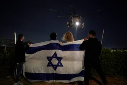 Gente sosteniendo una bandera israelí mira la llegada de un helicóptero que transporta a rehenes israelíes liberados por Hamás en el Centro Médico Sheba en Ramat Gan, Israel, el martes 28 de noviembre de 2023. Los mediadores internacionales trabajaban el miércoles 29 para ampliar la tregua en Gaza, con la esperanza de que Hamás, que gobierna el territorio, siguiera entregando rehenes a cambio de la liberación de prisioneros palestinos y más alivio de la ofensiva aérea y terrestre israelí. De lo contrario, el acuerdo expiraría en un día. (AP Foto/Leo Correa)
