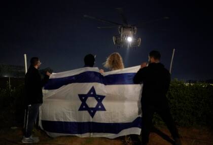 Gente sosteniendo una bandera israelí mira la llegada de un helicóptero que transporta a rehenes israelíes liberados por Hamas en el Centro Médico Sheba en Ramat Gan, Israel, el martes 28 de noviembre de 2023.