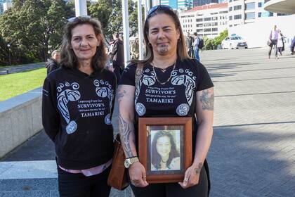 Gina, a la derecha, y Tanya Sammons muestran una foto de su hermana fallecida, Alva, a su llegada al parlamento en Wellington, Nueva Zelanda, antes de una disculpa a los sobrevivientes de abusos en centros estatales, religiosos y de acogida durante un periodo de siete décadas. (AP Foto/Charlotte Graham-McLay )