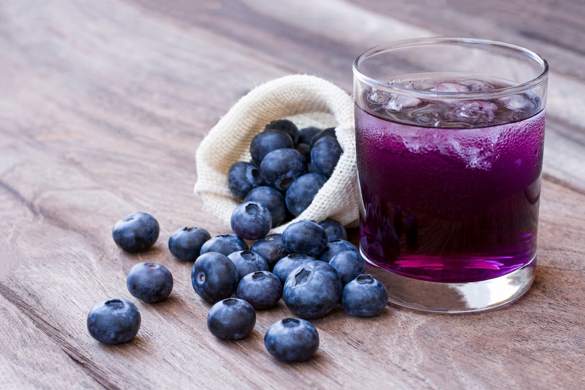Glass of blueberry juice and fresh blueberries fruit isolated on wooden table background.