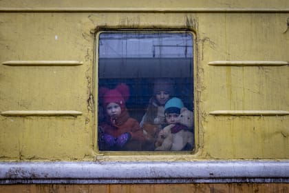 3 niños miran desde la ventana de un tren de carga utilizado para evacuar gente, en la estación de trenes de Kiev, Ucrania.