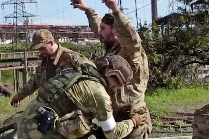 En esta foto tomada de un video publicado por el Servicio de Prensa del Ministerio de Defensa de Rusia el martes 17 de mayo de 2022, soldados rusos cachean a soldados ucranianos mientras son evacuados de la planta siderúrgica Azovstal sitiada en Mariupol
