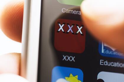 Hand holding smartphone, touching porn application icon on screen with thumb.