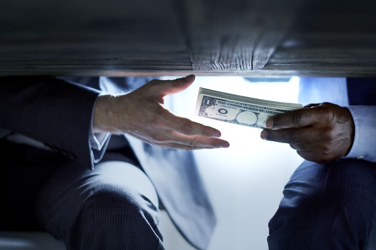Hands passing money under table corruption bribery