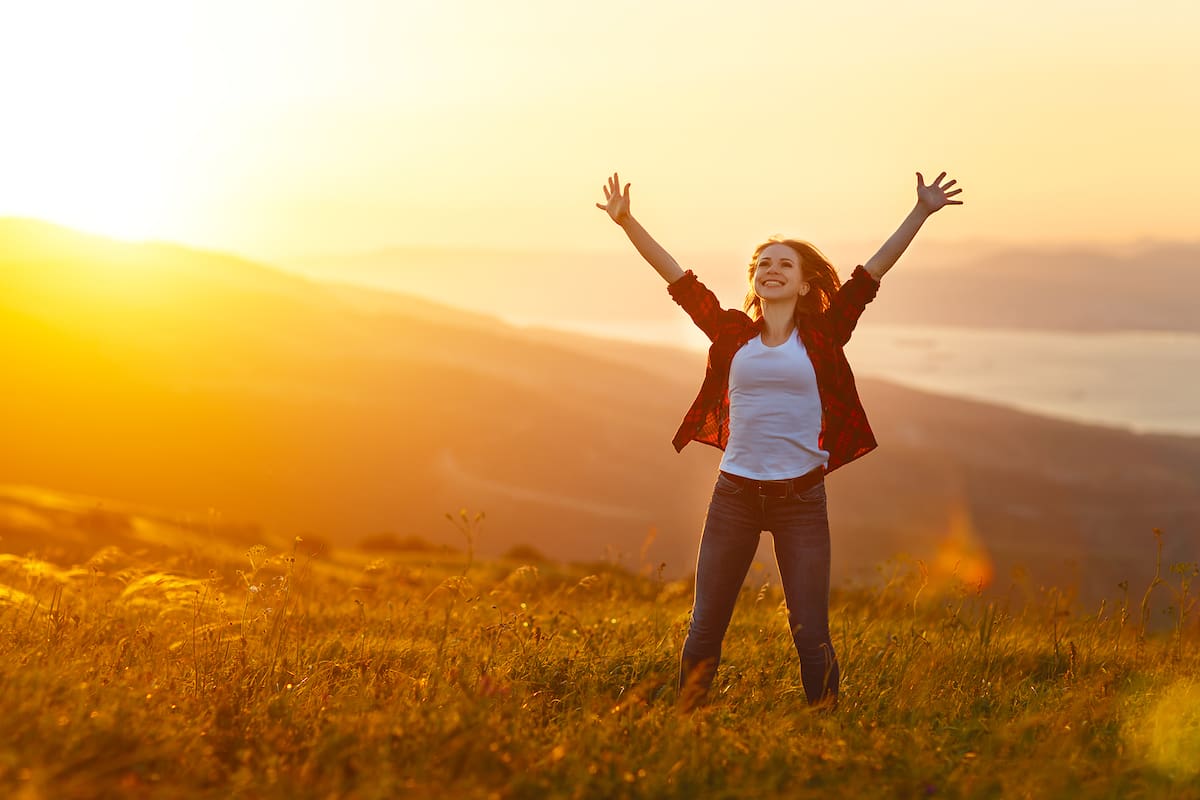 Happy woman on the sunset in nature in summer with open hands