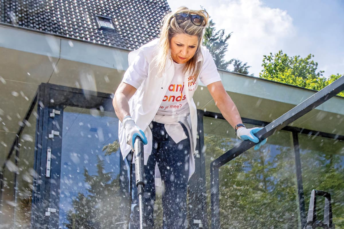 Hidrolavadora en mano y con guantes, la reina limpia los pisos del centro comunitario Cultuurhuis De Paulus, en la ciudad de Oegstgeest, donde asistió junto a su marido para hacer tareas de limpieza en el interior y los jardines del lugar.