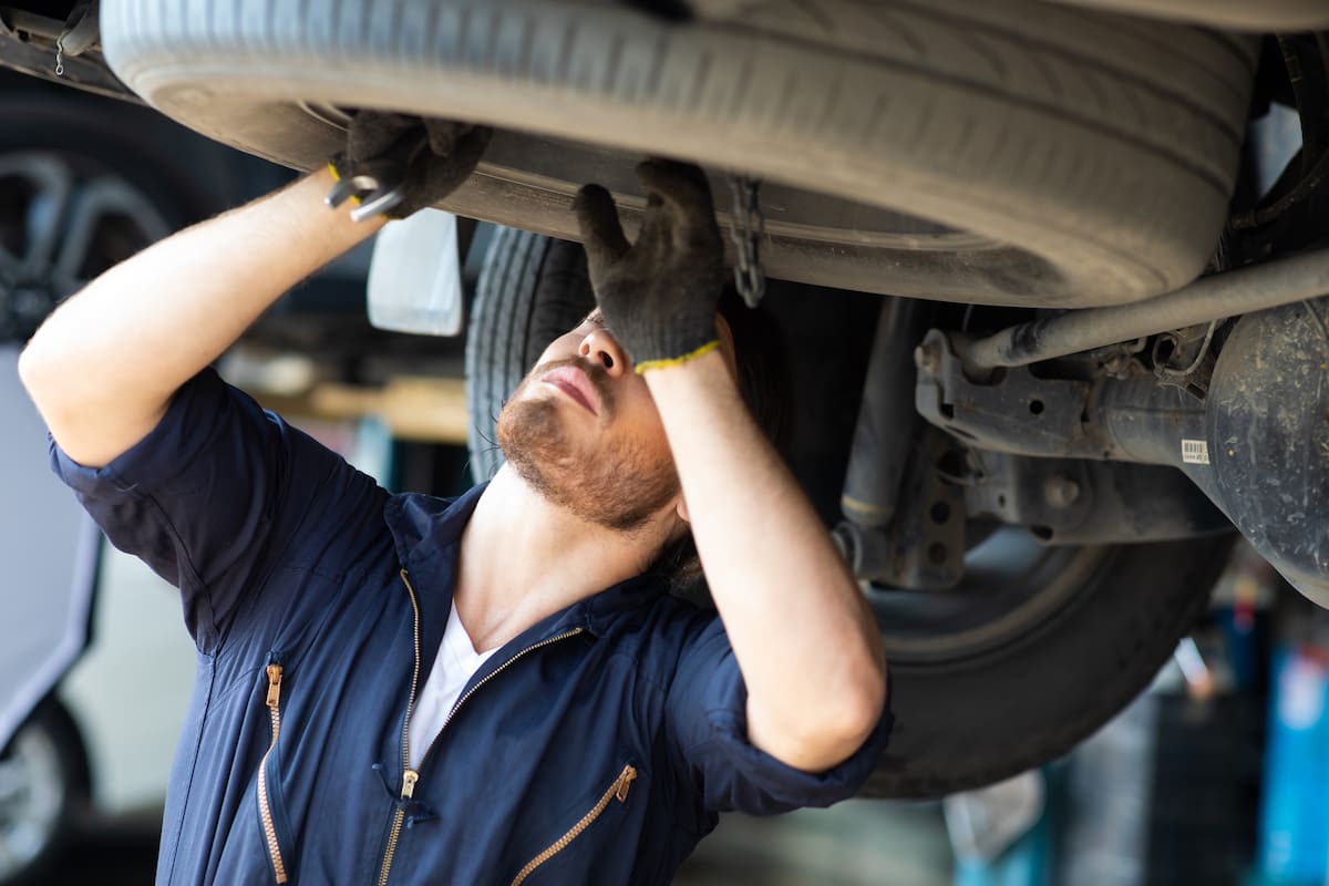 Hipster man mechanic working Under a Vehicle in a Car Service station. Expertise mechanic working in automobile repair garage.