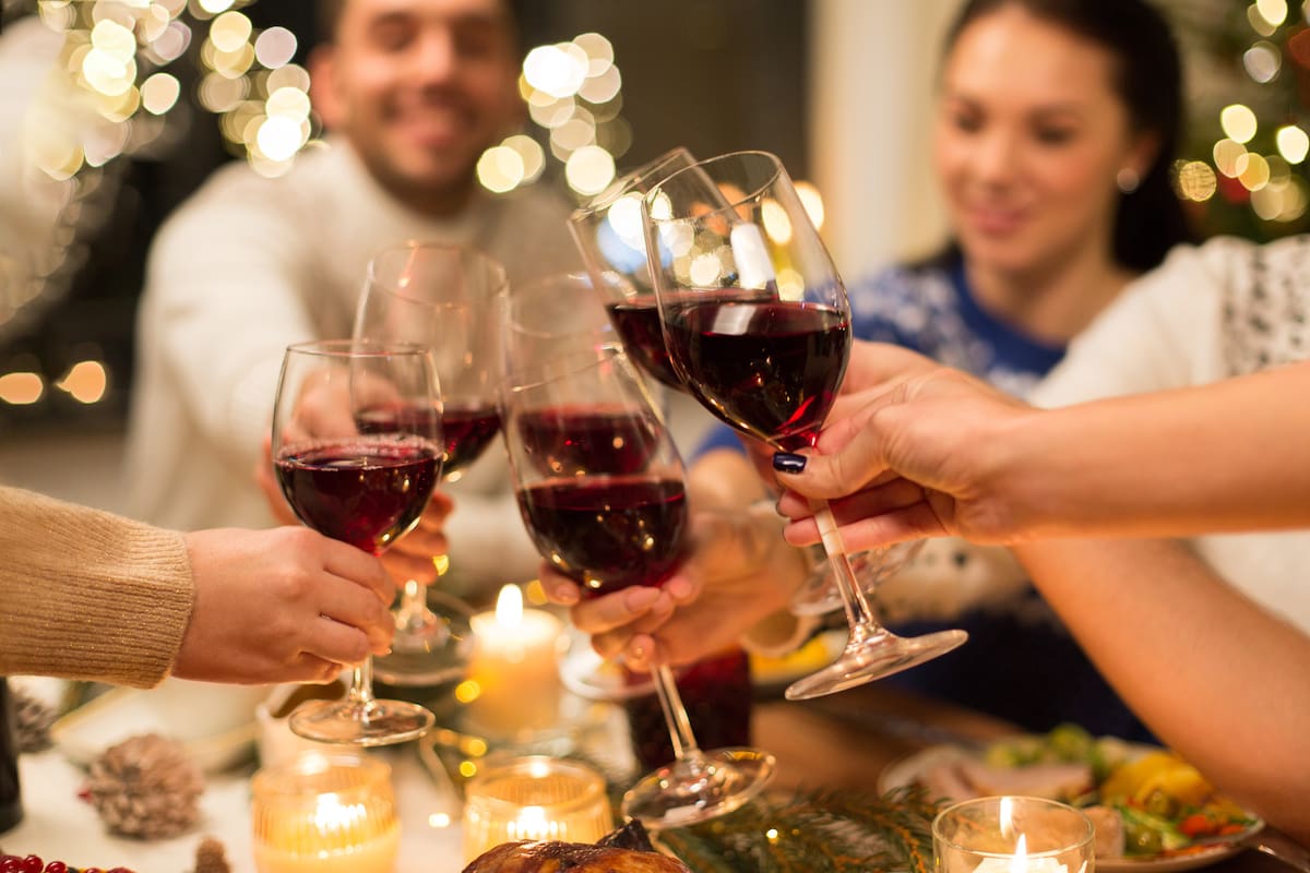 holidays and celebration concept - close up of happy friends having christmas dinner at home, drinking red wine and clinking glasses