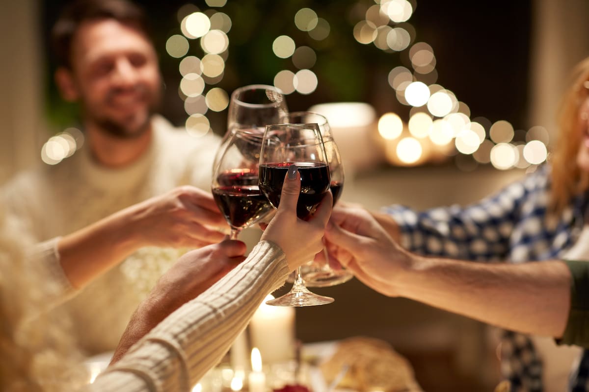 holidays, celebration and people concept - happy friends having christmas dinner at home drinking non-alcoholic red wine