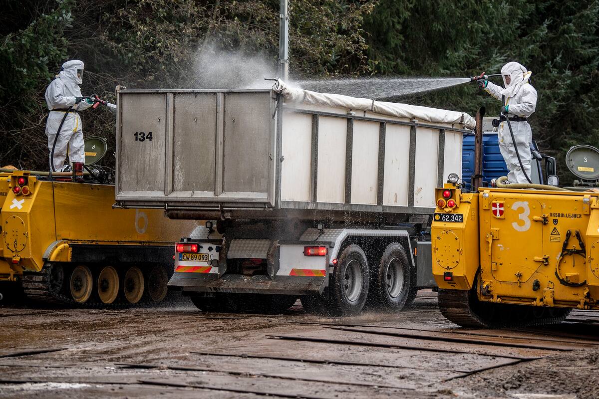 Hombres con trajes especiales desinfectan el contenedor de un camión mientras miembros de las autoridades sanitarias danesas asistidos por miembros de las Fuerzas Armadas eliminan visones muertos en un área militar cerca de Holstebro, Dinamarca, el 9 de noviembre de 2020