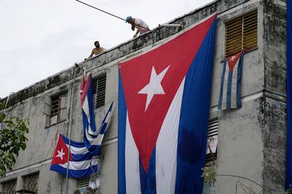 Hombres cuelgan banderas cubanas en las ventanas de la casa del dramaturgo y opositor Yunior García en un intento de evitar que se comunique con el exterior, mientras sostiene una flor desde una ventana, en La Habana, Cuba, el domingo 14 de noviembre de 2021