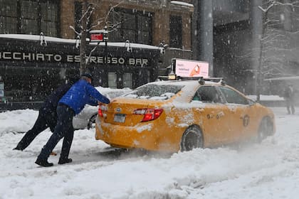 Hombres empujan un taxi que quedó varado en la nieve, en Nueva York