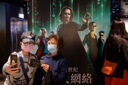 HONG KONG, CHINA - 2021/12/22: Moviegoers take a selfie in front of a Warner Bros. Pictures' movie banner for the premiere screening of franchise  The Matrix Resurrections film, played by Keanu Reeves, at a movie theater in Hong Kong. (Photo by Budrul Chukrut/SOPA Images/LightRocket via Getty Images)